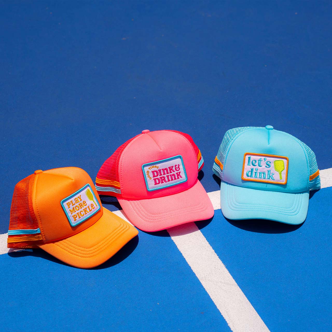 The Swinton Pickleball Dink & Drink Pink Foam Snapback Hat features a playful embroidered patch and an adjustable snap closure, shown here on a bright blue pickleball court.
