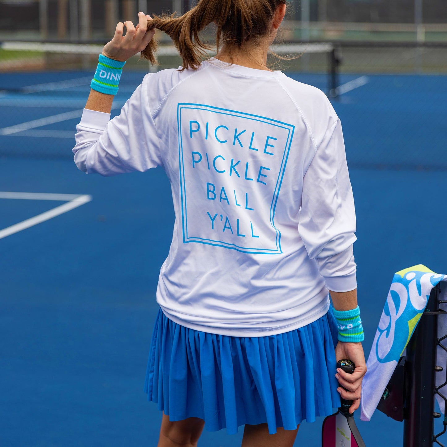 A woman holds a tennis racket, wearing Swinton Pickleball’s Pickle Pickle Ball Y'all UPF 50+ long sleeve water shirt for sun protection and moisture-wicking comfort.