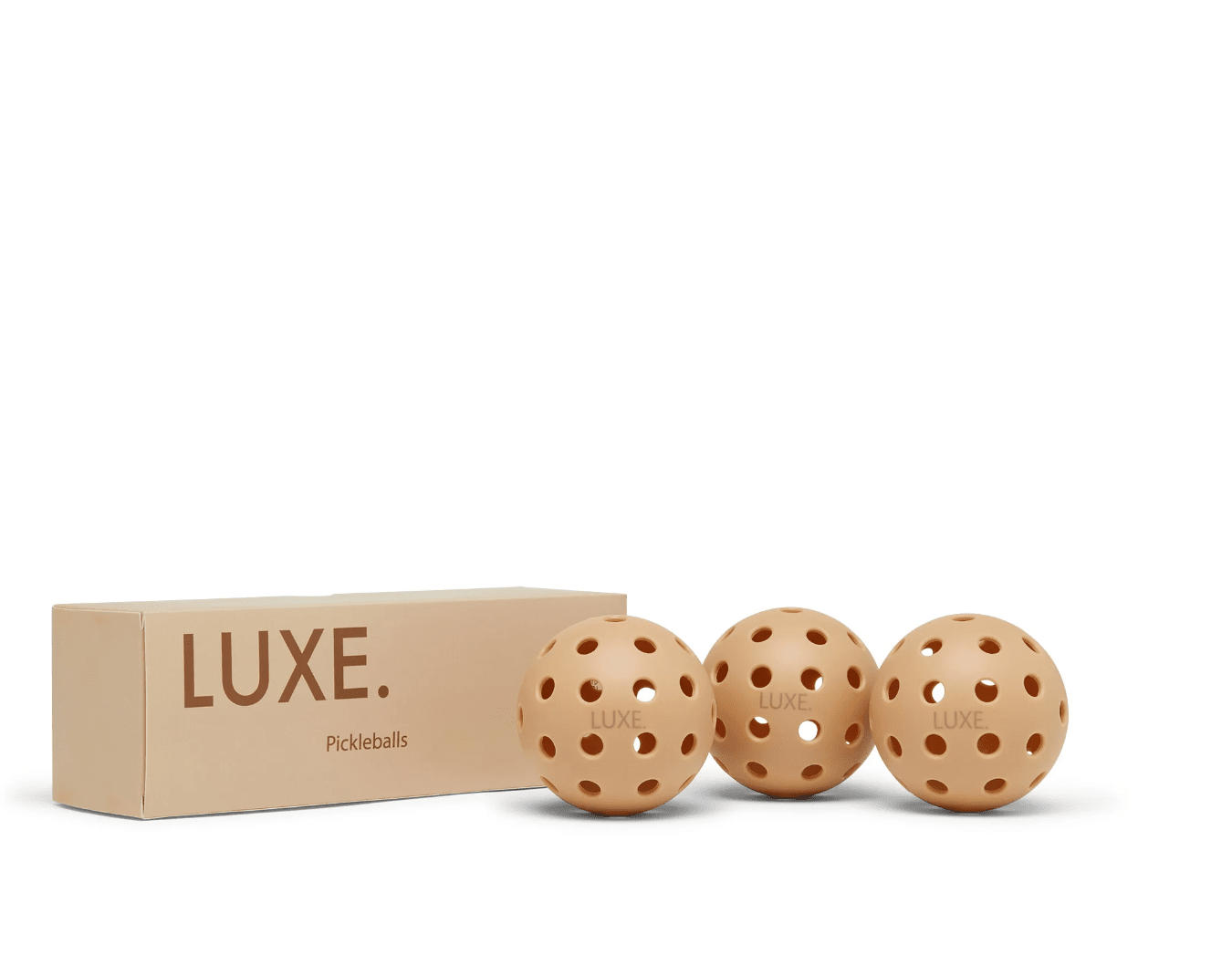 Three tan LUXE Pickleball pickleballs, each with 40 holes, are placed beside a box.