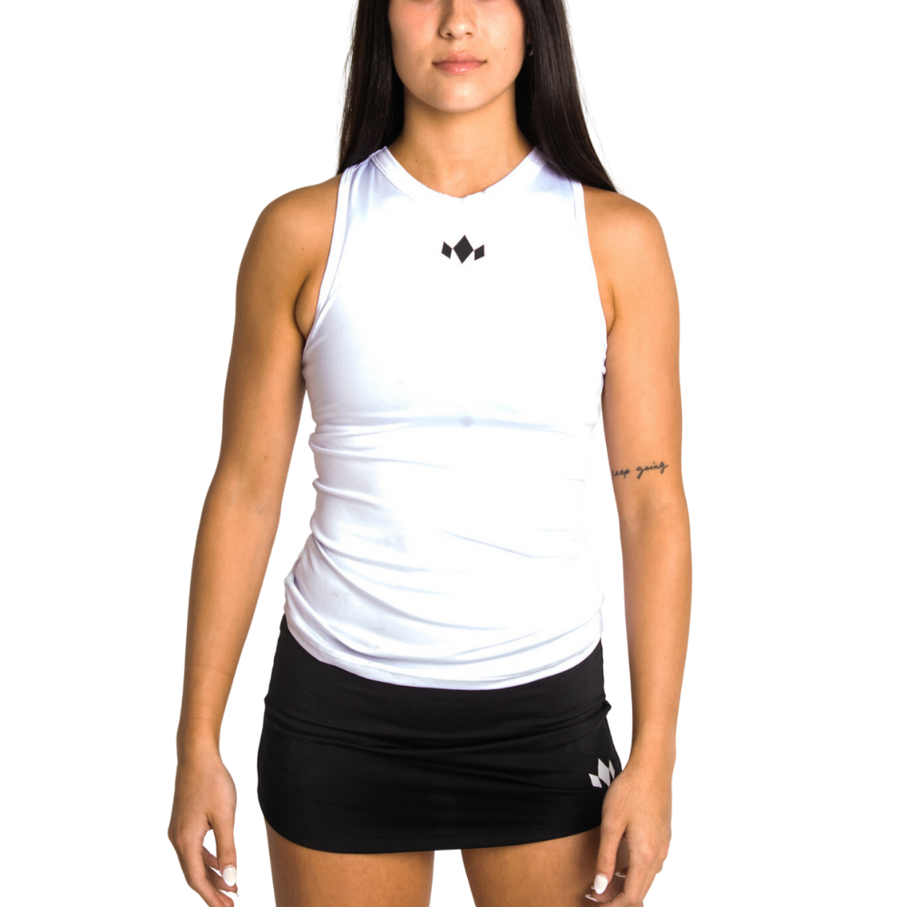 A woman with long dark hair wears the Diadem Sports Team Essential Highneck Tank, a sweat-wicking white athletic top, paired with a black mini skirt. Both feature small black logos. She faces forward against a plain white background, tattoo visible on her left forearm.