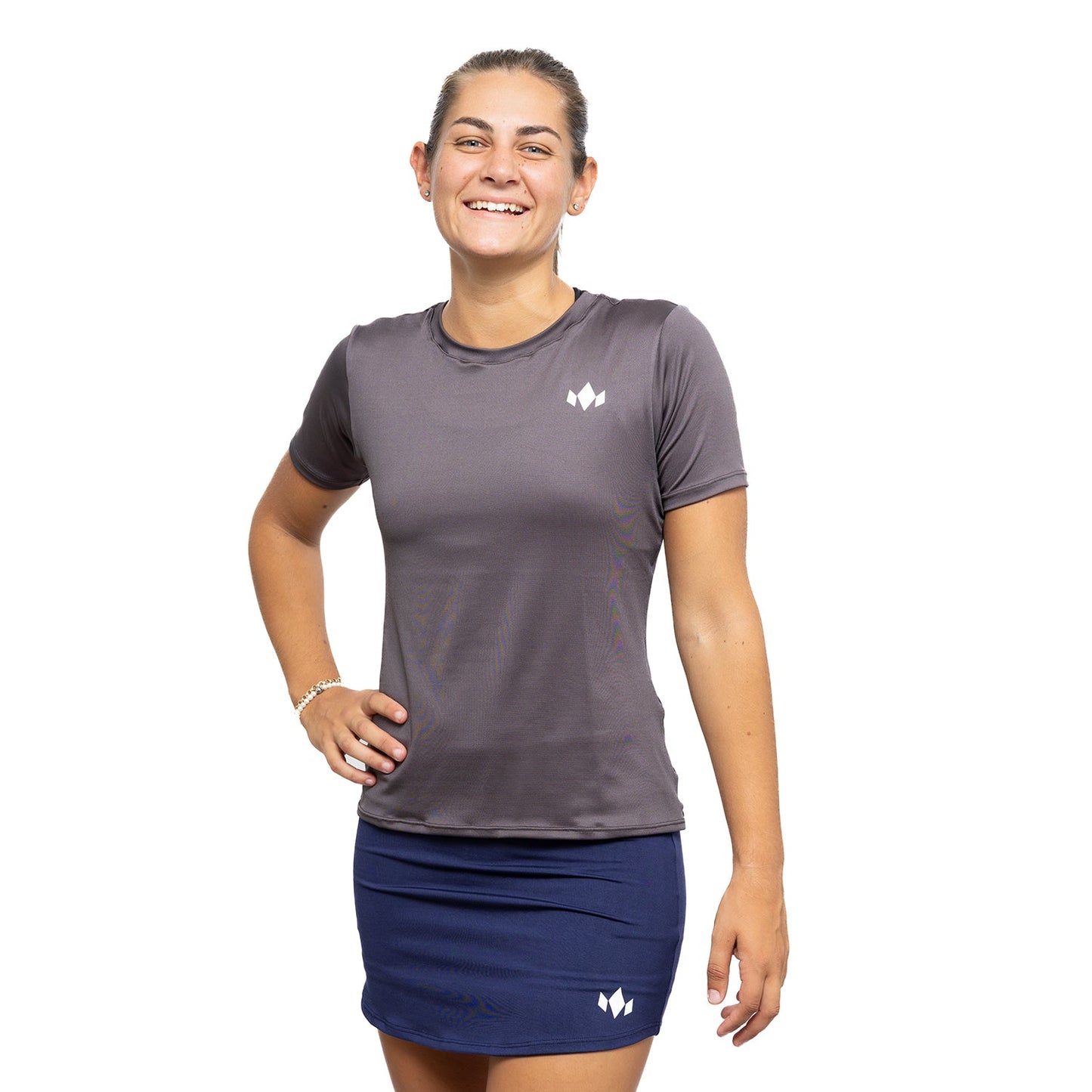 A smiling woman poses against a white background, wearing the Diadem Sports Team Women's Essential Crewneck athletic shirt in gray and a navy-blue skirt with small white logos. Her hair is tied back, one hand on her hip and the other by her side.