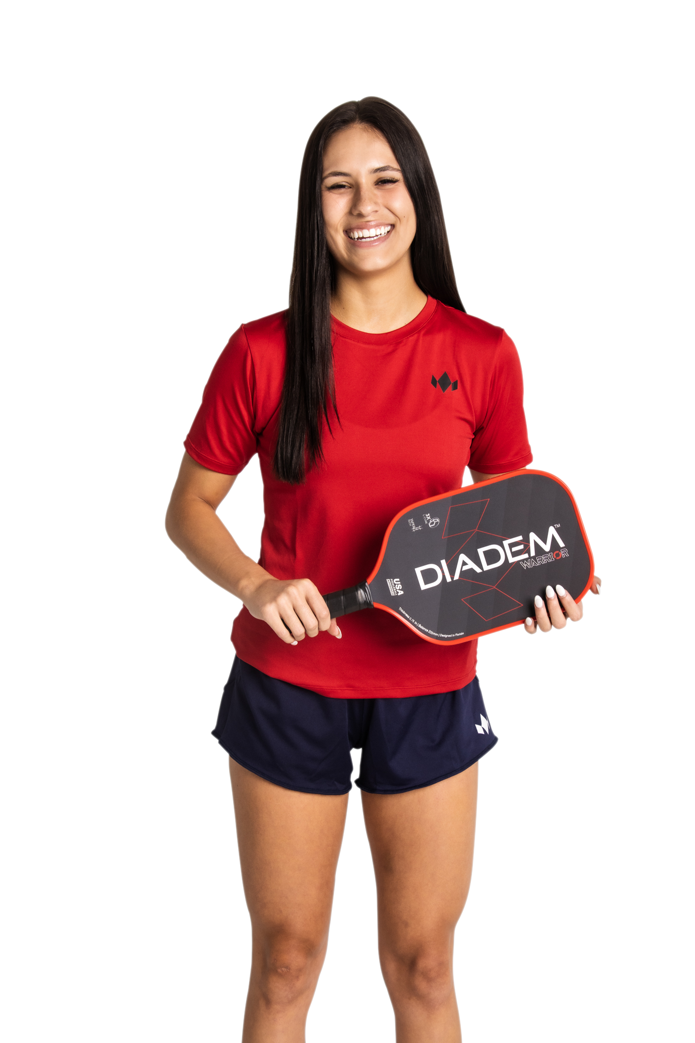 A young woman with long dark hair smiles while holding a Diadem pickleball paddle. She wears the Diadem Sports Team Women's Essential Crewneck red athletic shirt and navy blue shorts, standing against a plain white background.