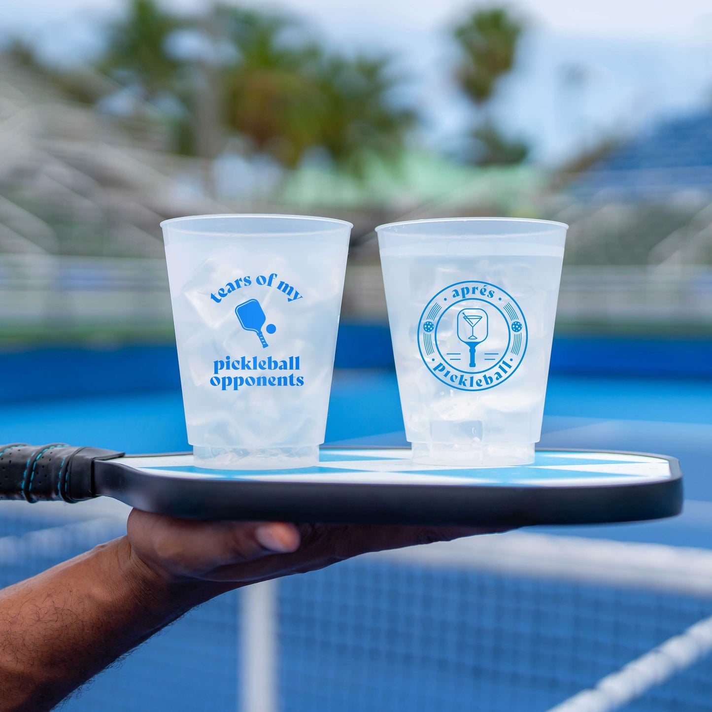 A hand holds a tray with two Swinton Pickleball "Tears of my Pickleball Opponents" reusable party cups—ideal for your next pickleball gathering.
