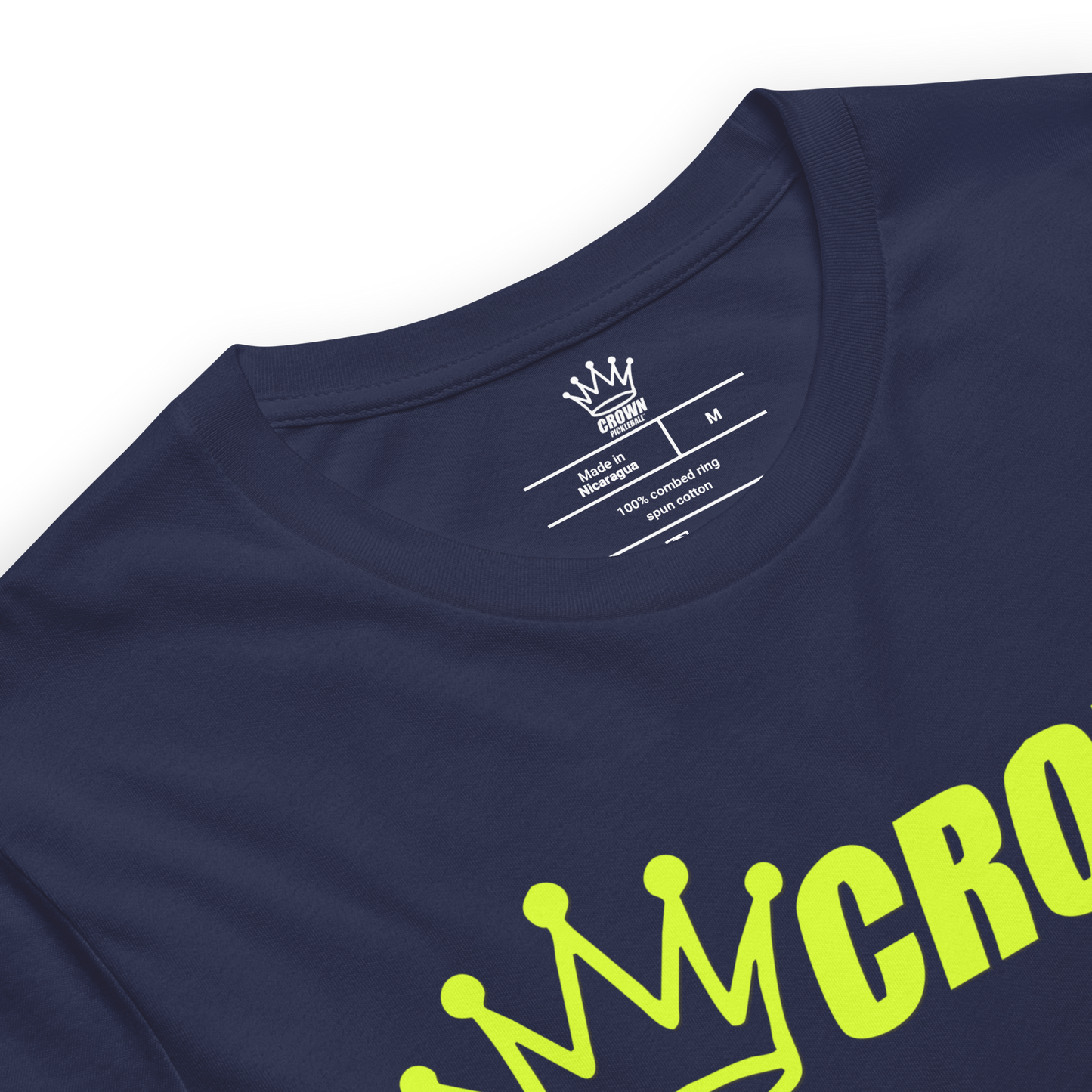 Close-up of the CROWN PICKLEBALL - Logo Shirt (Navy) by Crown Pickleball, featuring a bold yellow crown graphic and partial “CROWN” text on navy fabric. The inside neck label shows the Crown Pickleball logo, size M, and care details in white.