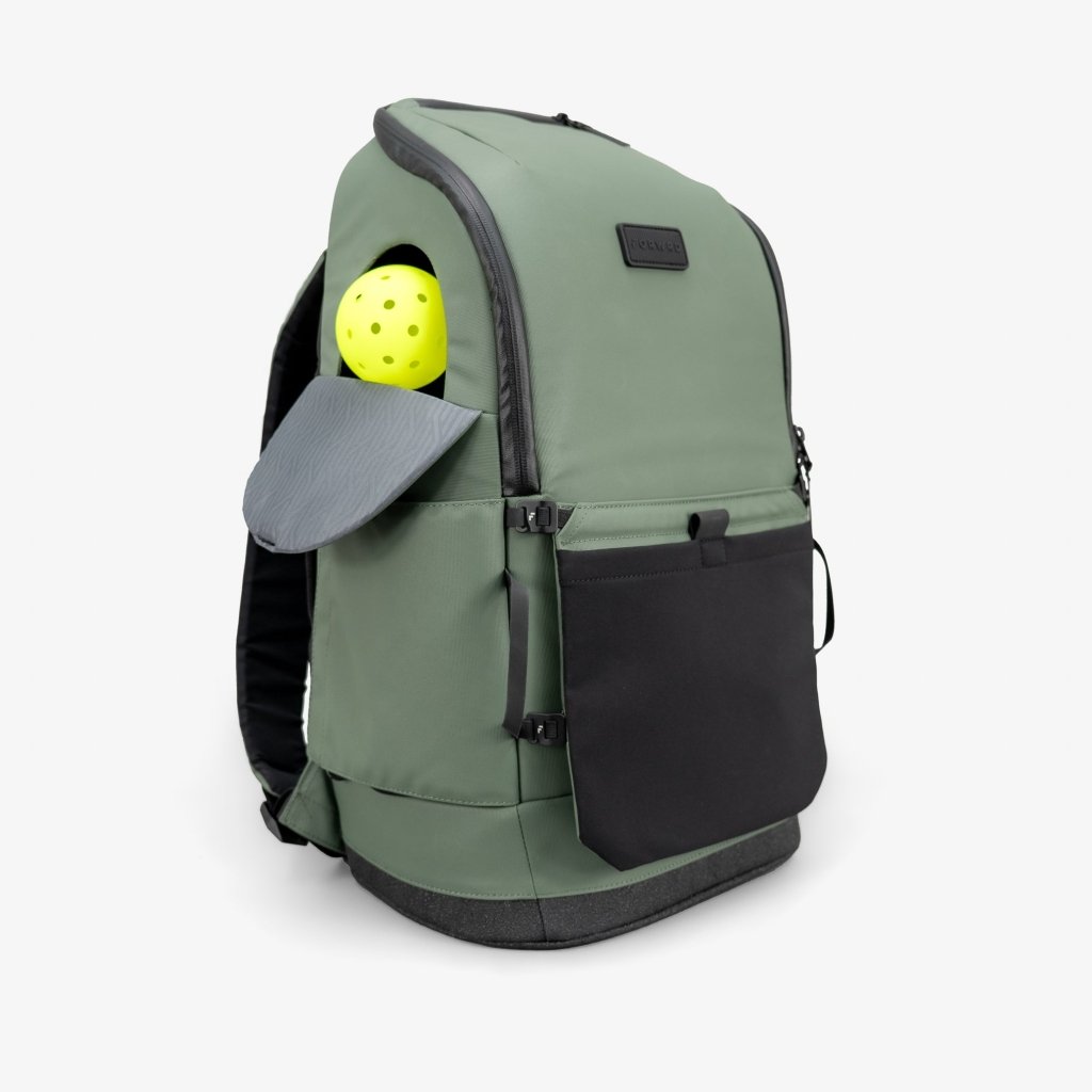 The FORWRD Court Caddy Front Paddle Sleeve in sage green with black accents stands upright. The left sleeve holds a yellow pickleball and gray paddle. Features: large front pocket, black rubber base, and padded shoulder straps.