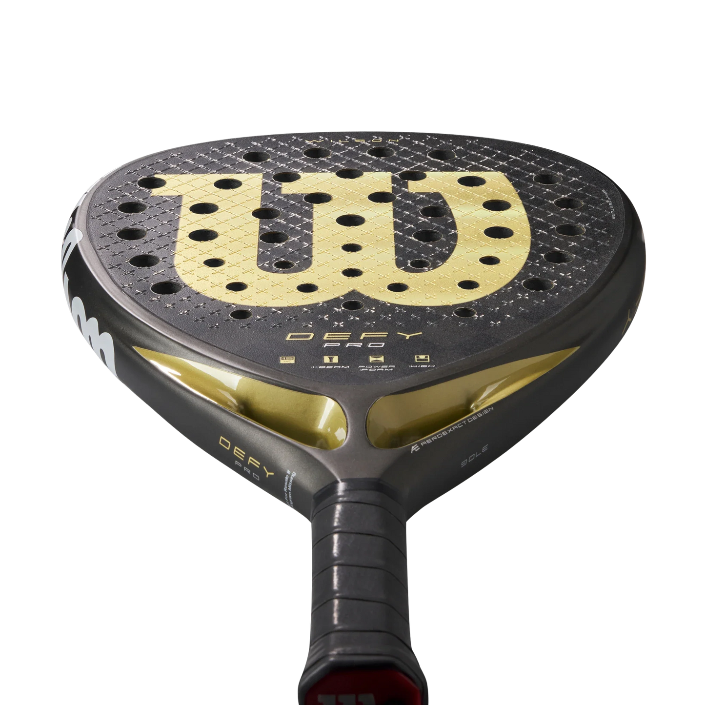 Close-up of the Wilson Defy Pro V1 Padel Racket by Padel USA, showcasing its black and gold design, large gold W logo on the 15K Carbon Face, black grip tape handle, and DEFY and Wilson branding on the throat against a white background.