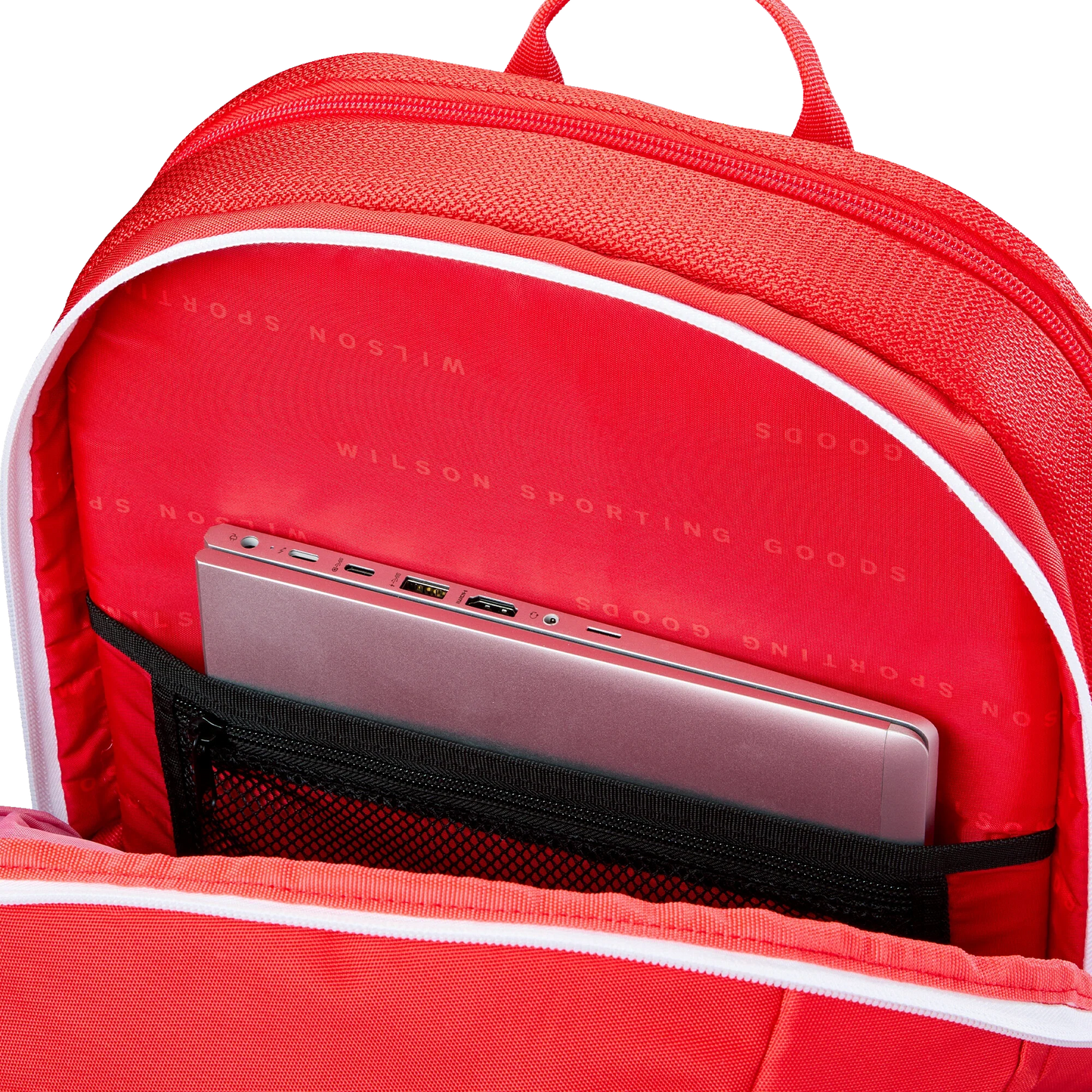 A close-up of the Wilson Tour Red Padel Backpack from Padel USA shows a padded compartment with a mesh pocket holding a closed silver laptop. The red interior lining features “WILSON SPORTING GOODS” in white, combining style and function.