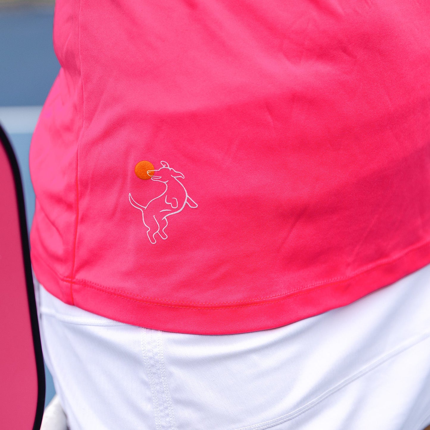 A close-up of someone wearing the Swinton Pickleball Women's Pickleball Performance Tank in hot pink, paired with white shorts. A hint of a pink tennis racket appears on the left.