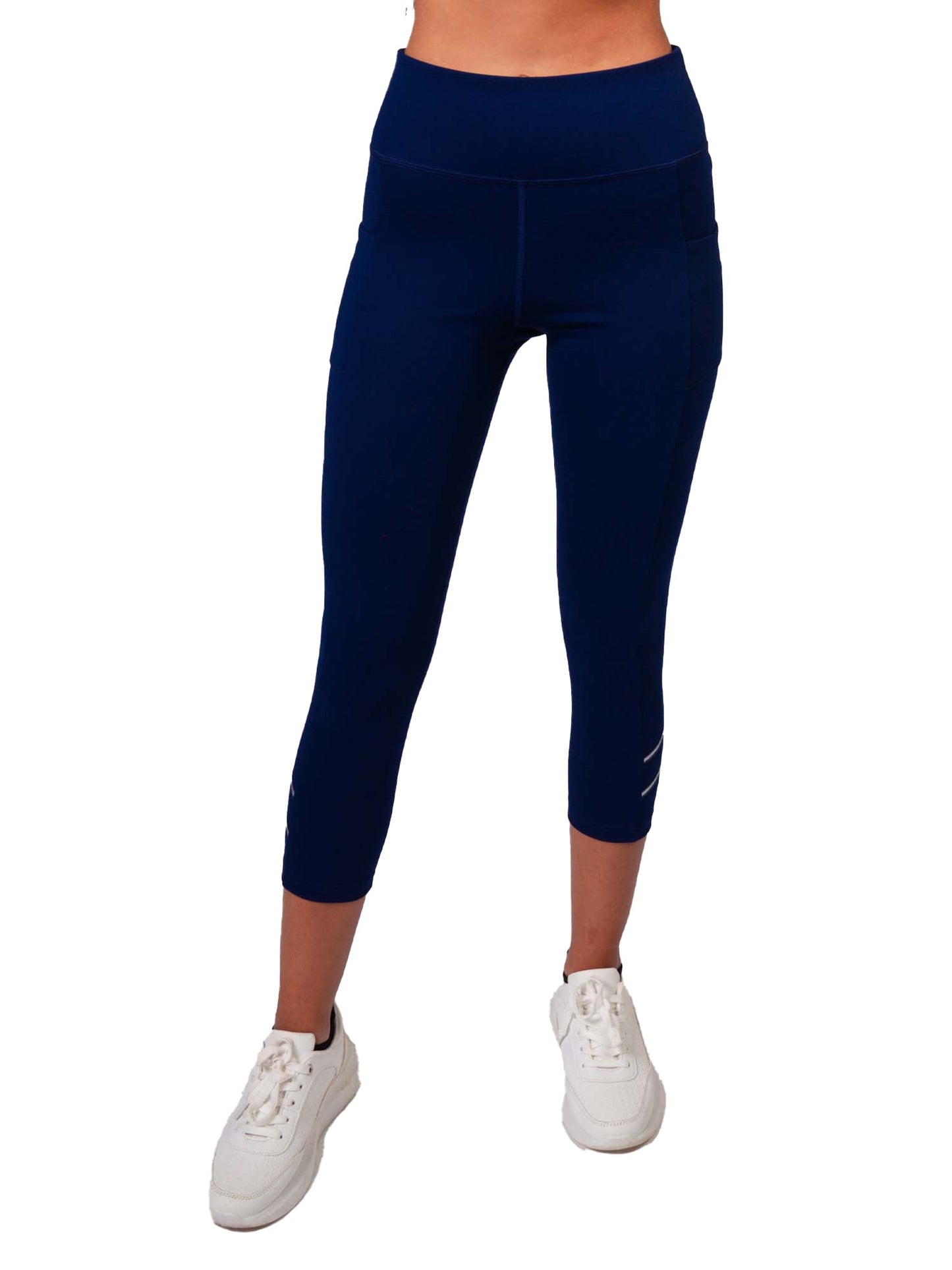 A person is shown from the waist down wearing inPhorm NYC Zone Capri Legging - Ink/Silver, high waisted and moisture wicking, reaching just below the knees, paired with white sneakers against a white background.